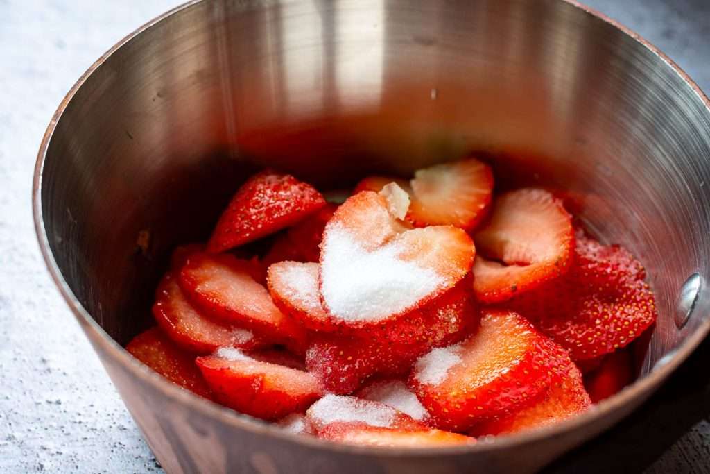 Sliced strawberries and sugar in a small copper pan.