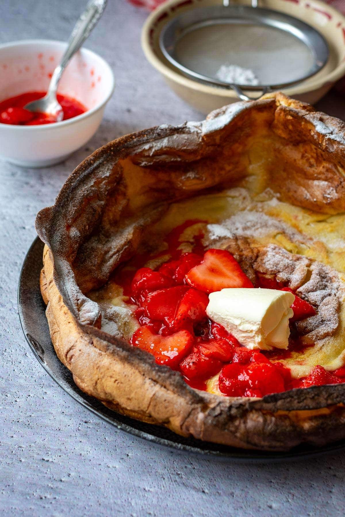 Puffy German pancake on a black plate topped with strawberry compote and creme fraiche.