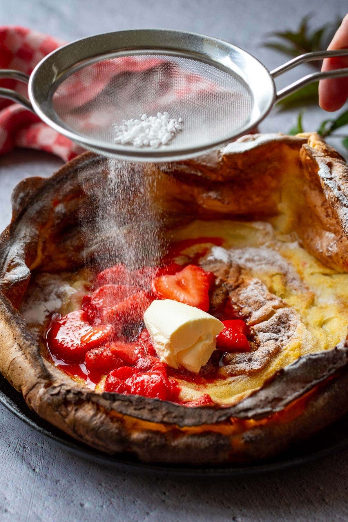 Dusting strawberry Dutch Baby With sugar.