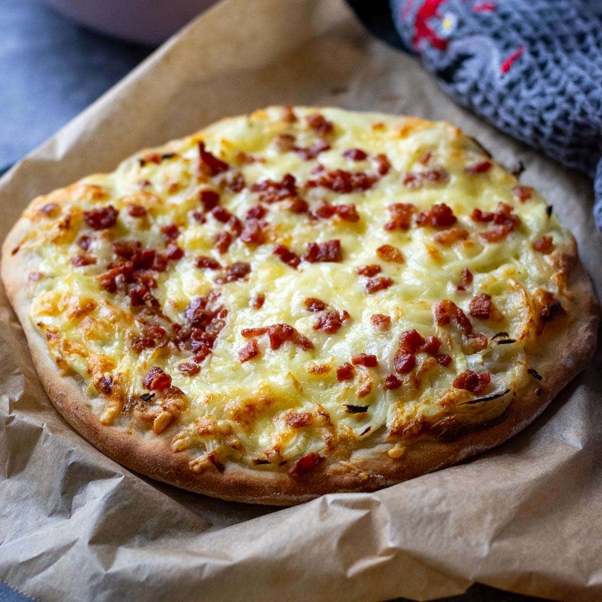 Sour cream pizza with onion and bacon on a large sheet of parchment paper.