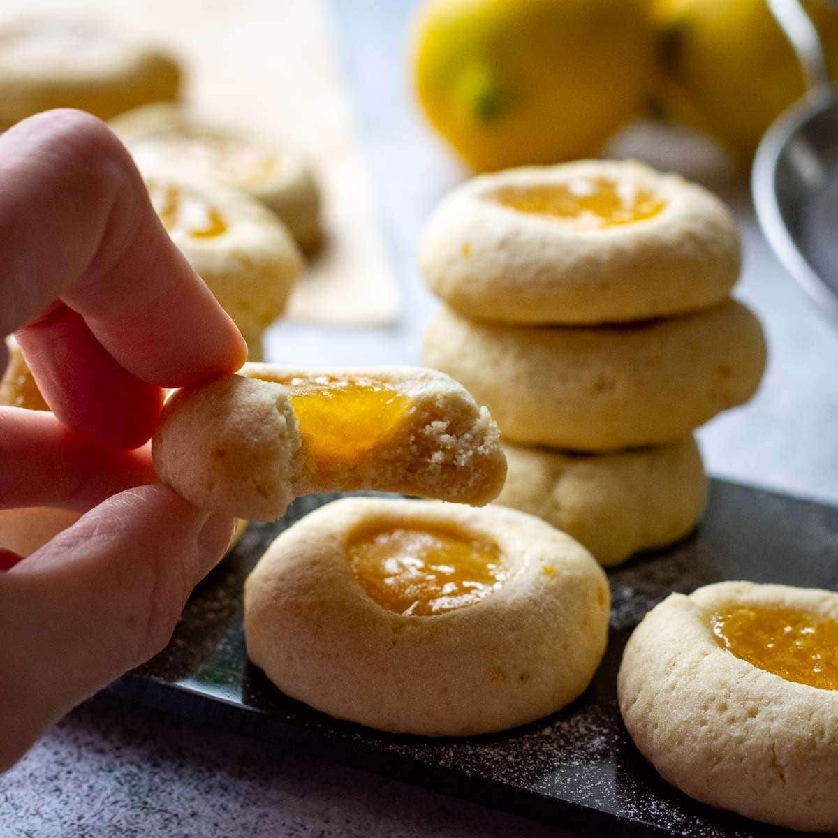 Lemon Thumprint Cookies With Lemon Curd on a black board with one cookie being picked up.
