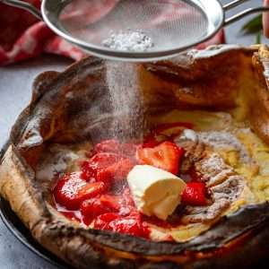 Powdered sugar being sprinkled on top of strawberry dutch baby.