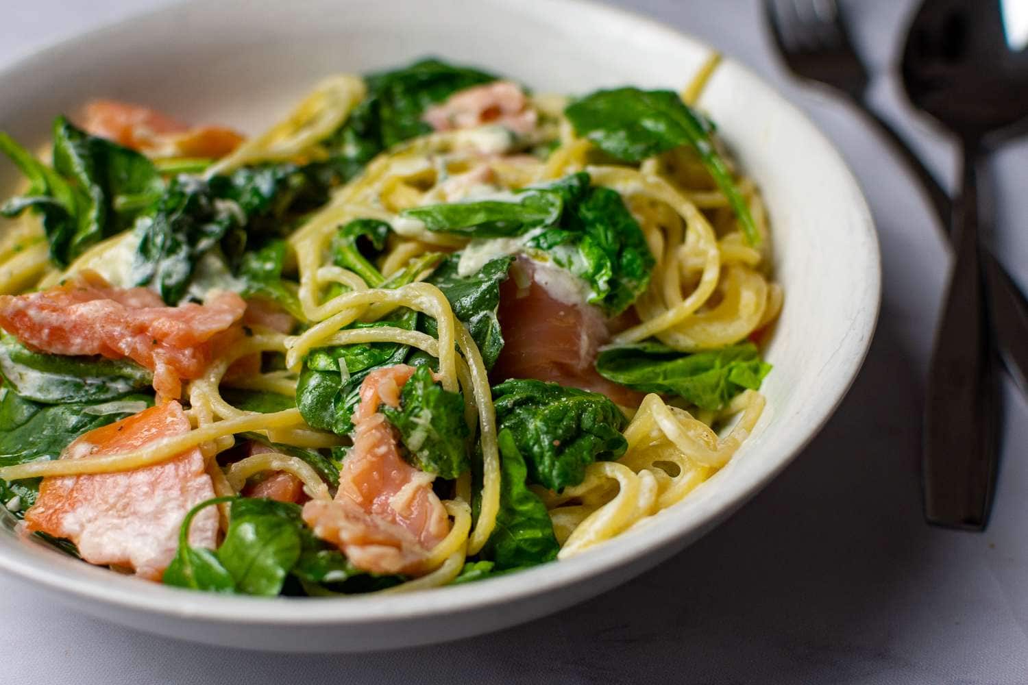 Smoked salmon and spinach pasta in white bowl.