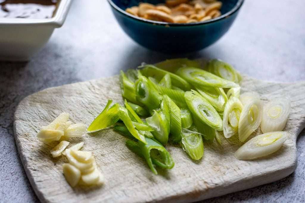 Sliced garlic and spring onion on a small chopping board.