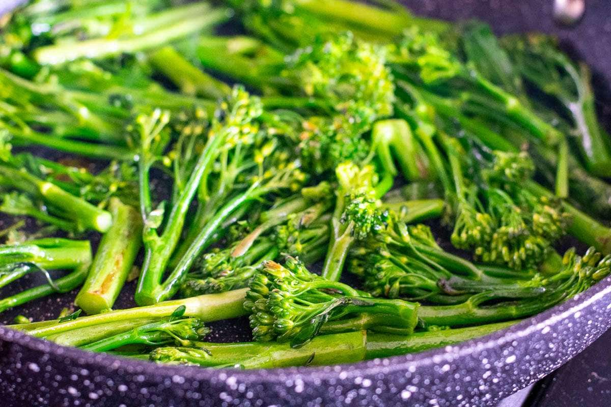 Frying tenderstem broccoli in a large frying pan.