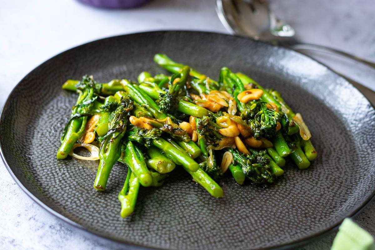 Stir fried tenderstem broccoli with yster sauce served on a large black plate.