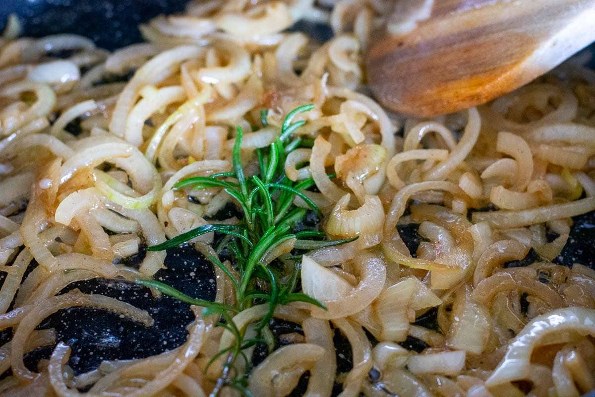 Sauteed onions in a frying pan with a sprig of rosemary.