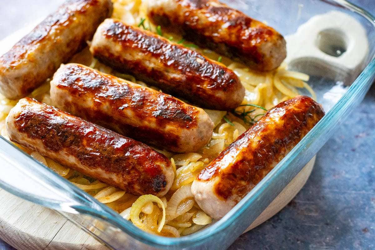 Onions and sausages in a glass baking tray.