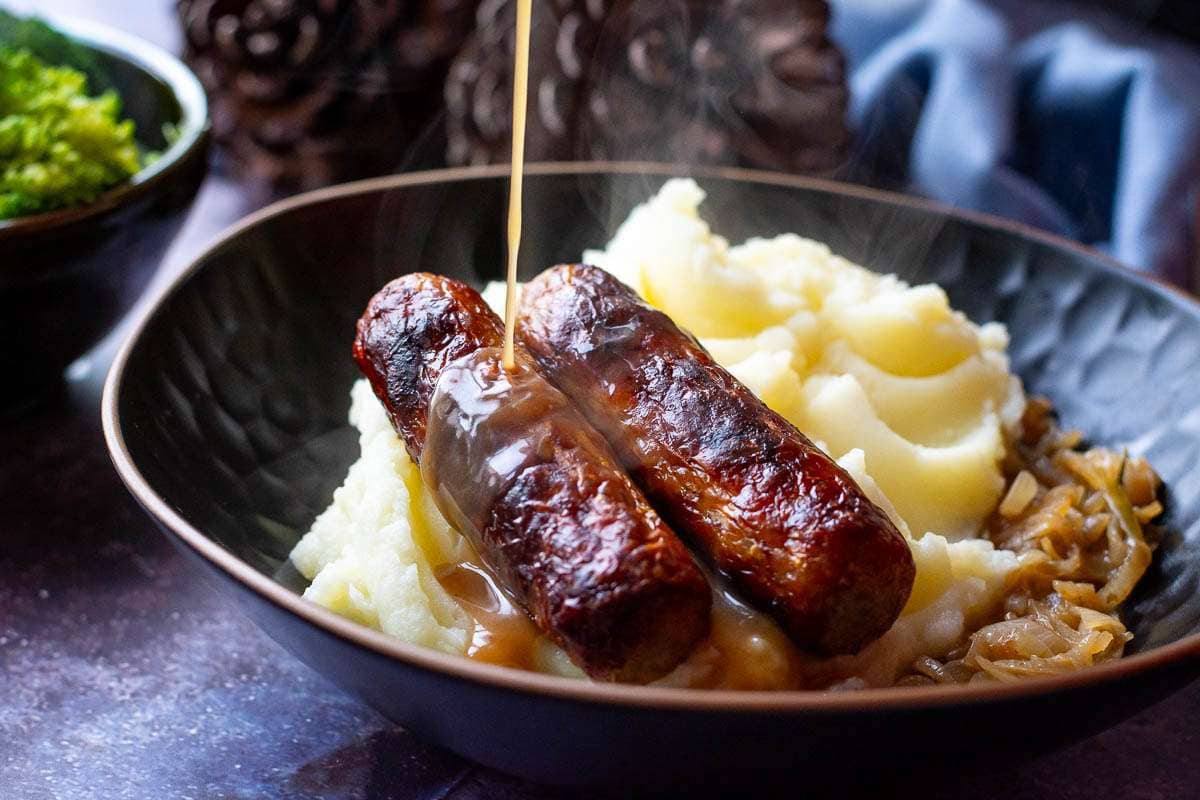 Onion gravy being poured over the sausages and potato mash.