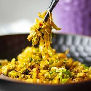 Stir fried savoy cabbage with chilli and garlic being picked up from a bowl with chopsticks.