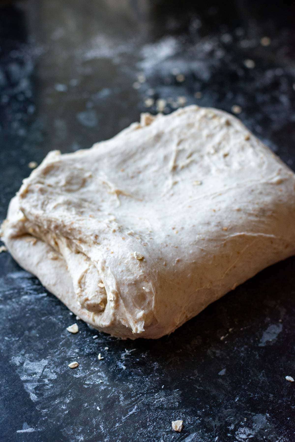 Oats being folded into the sourdough on a kitchen surface.