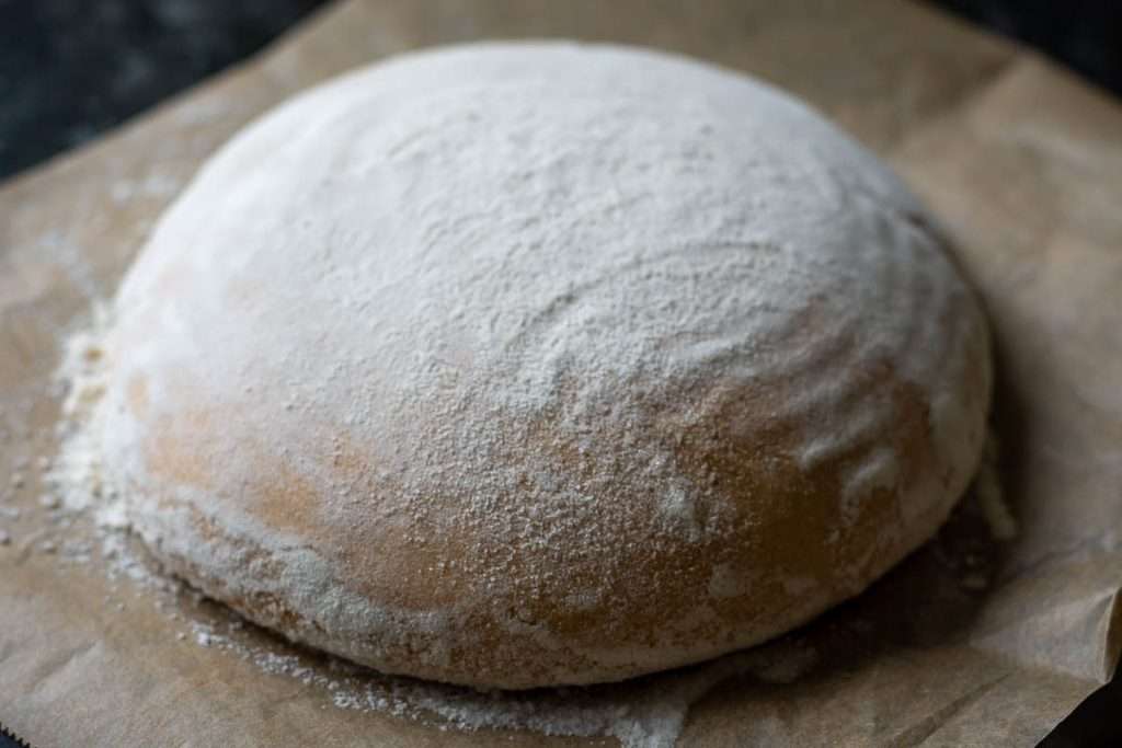 Pumpkin dough inverted out of the proofing basket onto a large sheet of parchment paper.