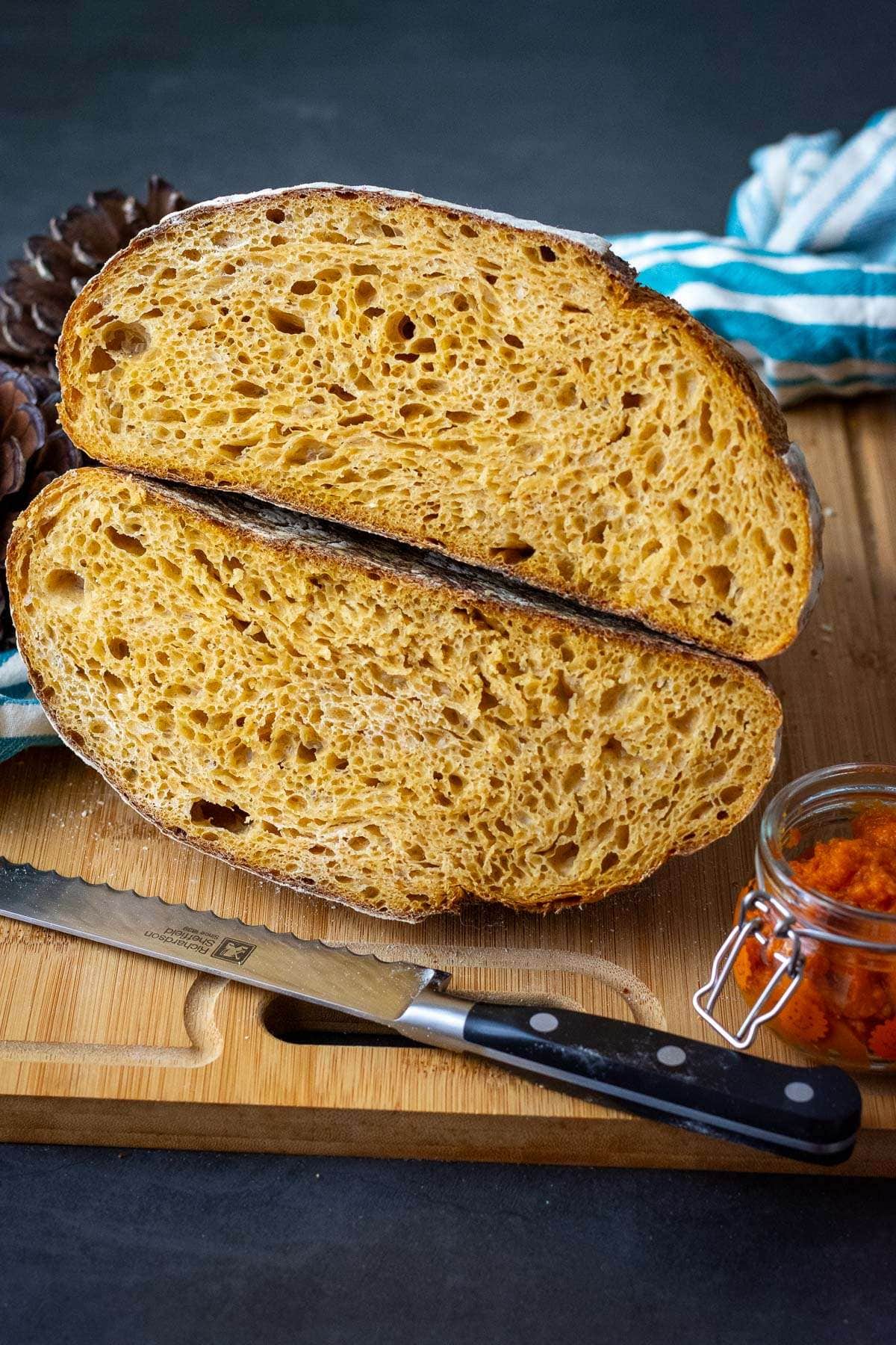Pumpkin Sourdough Bread cut in half and stacked on top of each over on a wooden board.