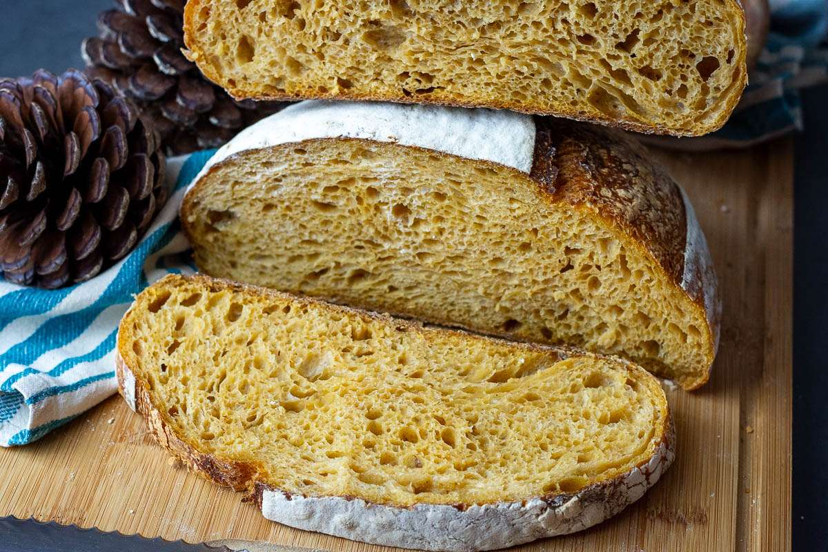 a slice of pumpkin sourdough bread on a large wooden cutting board.