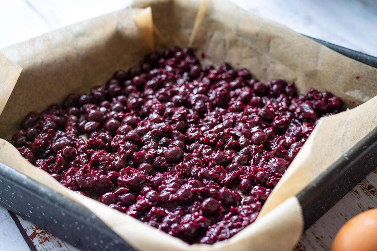 Blackcurrants in a single layer at the bottom of the lined baking tray.