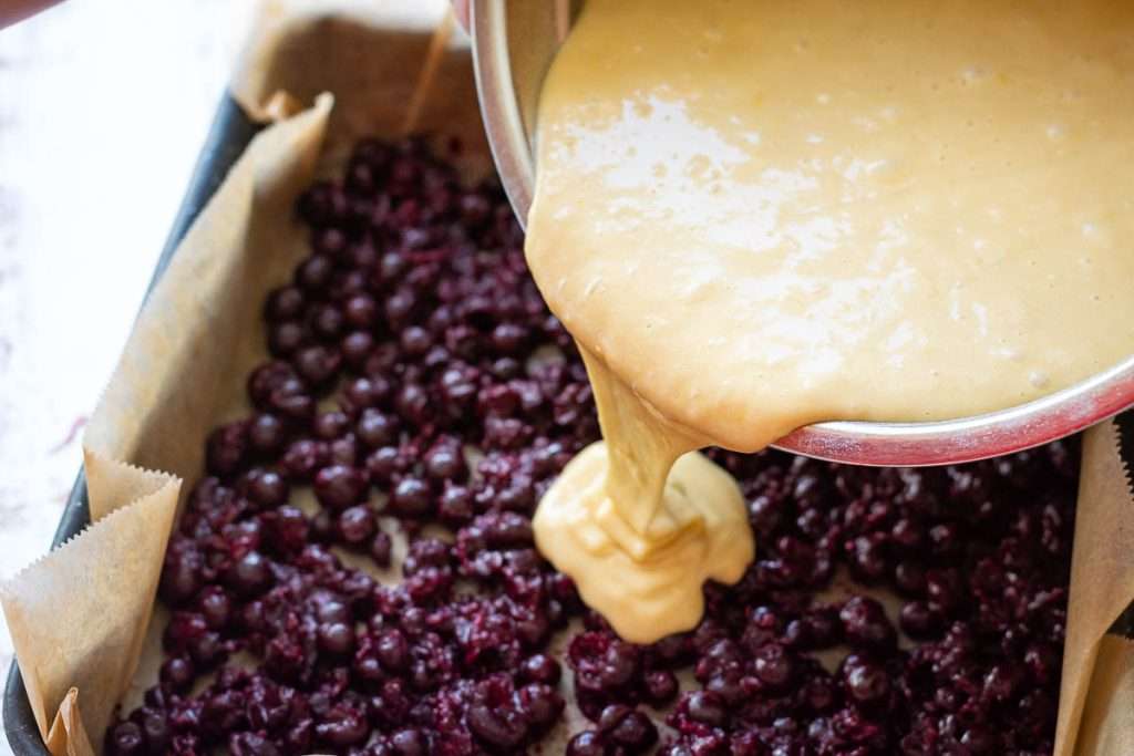Pouring the cake batter over the blackcurrants.