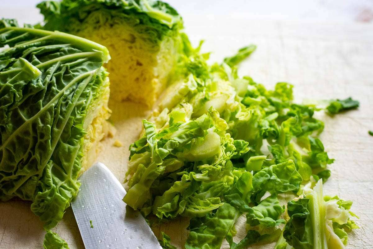 Shredding Savoy cabbage on a wooden chopping board.