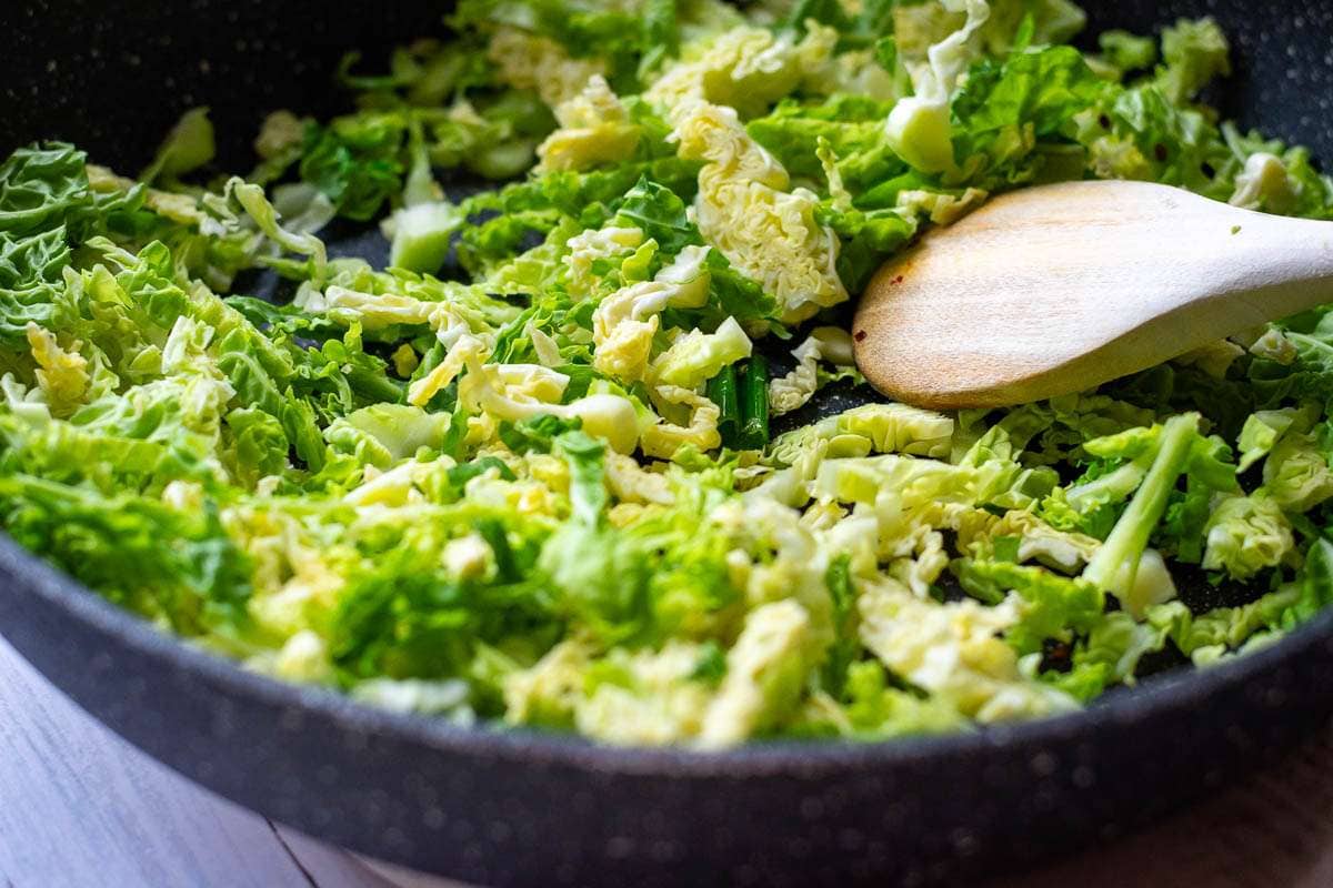 Shredded savoy cabbage added to the garlic, chilli and spring onion in the pan.