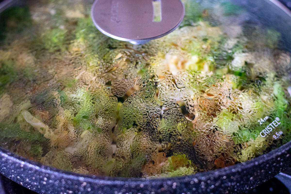 Savoy Cabbage stir fry cooking in a large frying pan with a lid on.