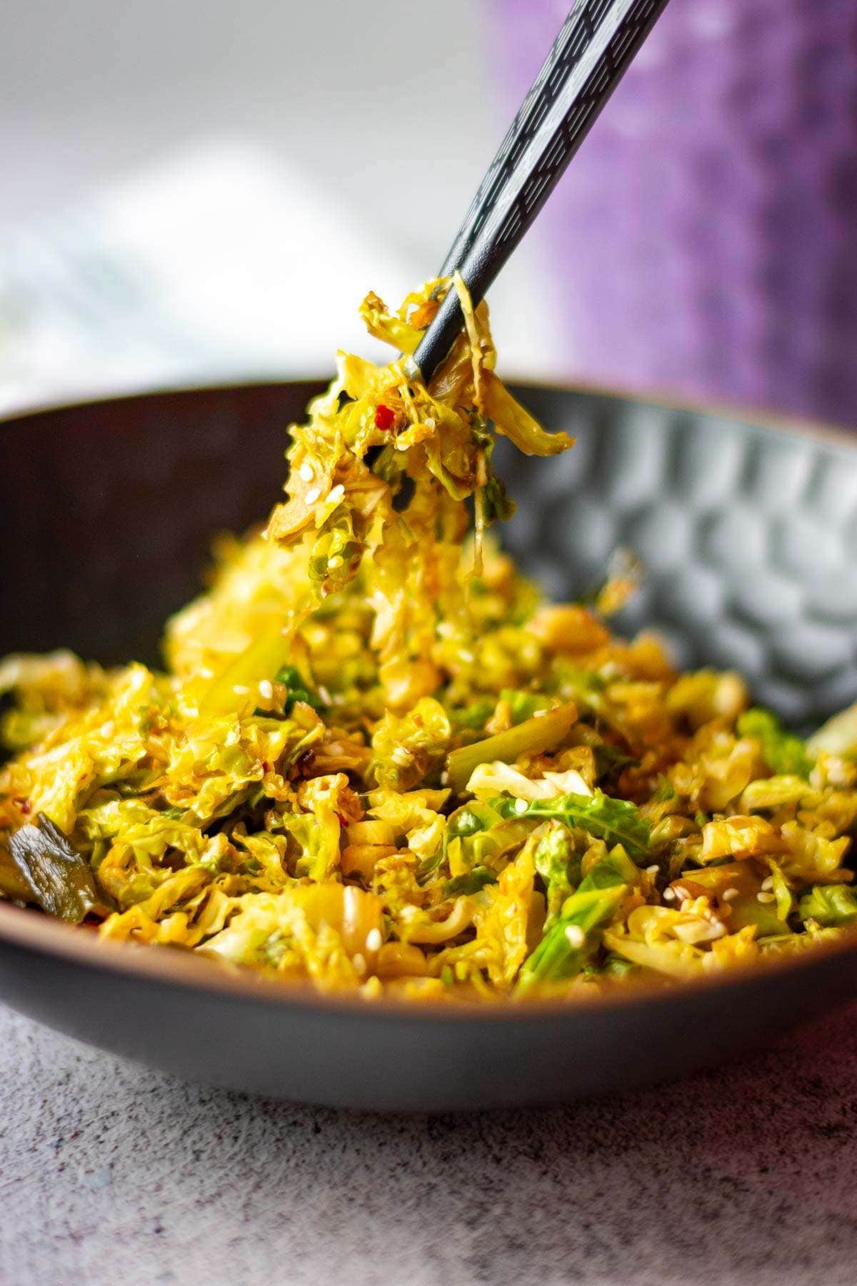 Stir fried savoy cabbage with chilli and garlic being picked up from a bowl with chopsticks.