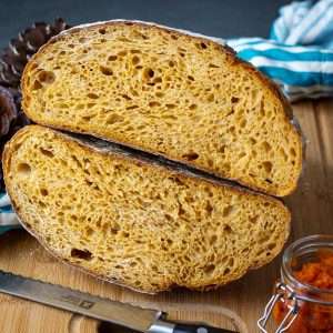 Pumpkin Sourdough Bread cut in half and stacked on top of each over on a wooden board.
