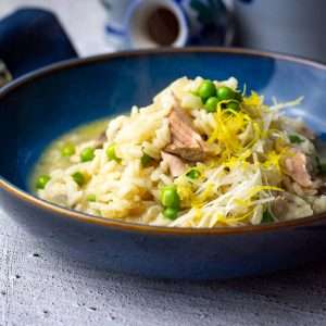 Salmon and pea risotto in a black bowl on a concrete surface.