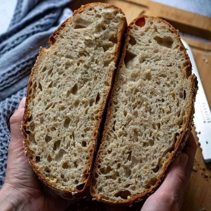Two honey oat sourdough bread halves held by two hands.