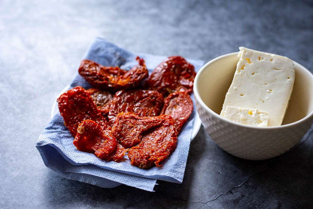 Sundried tomatoes on a paper towel and feta in small bowl,
