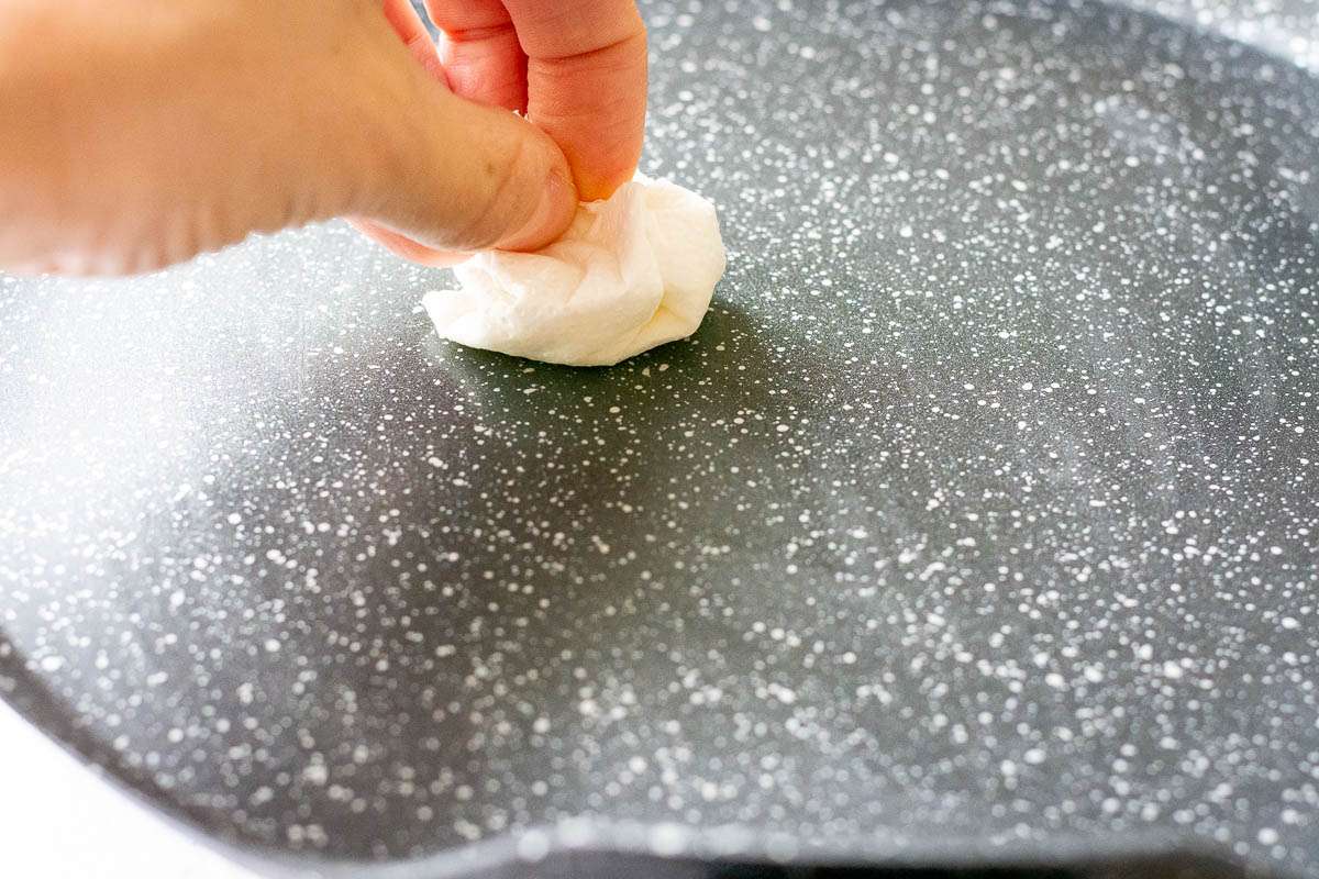 Greasing the crepe pan with a piece of paper towel soaked in oil.