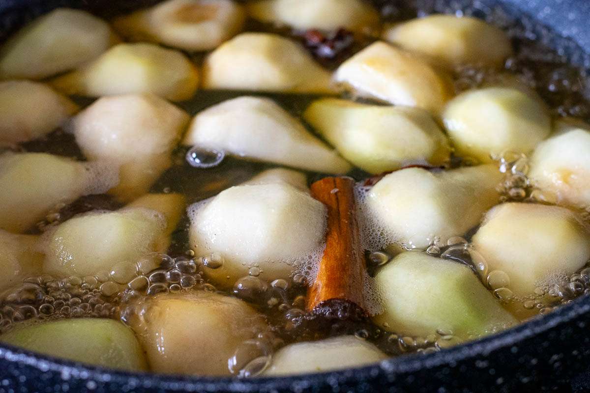 Pear quarters stewing in a lightly spiced poaching liquid.
