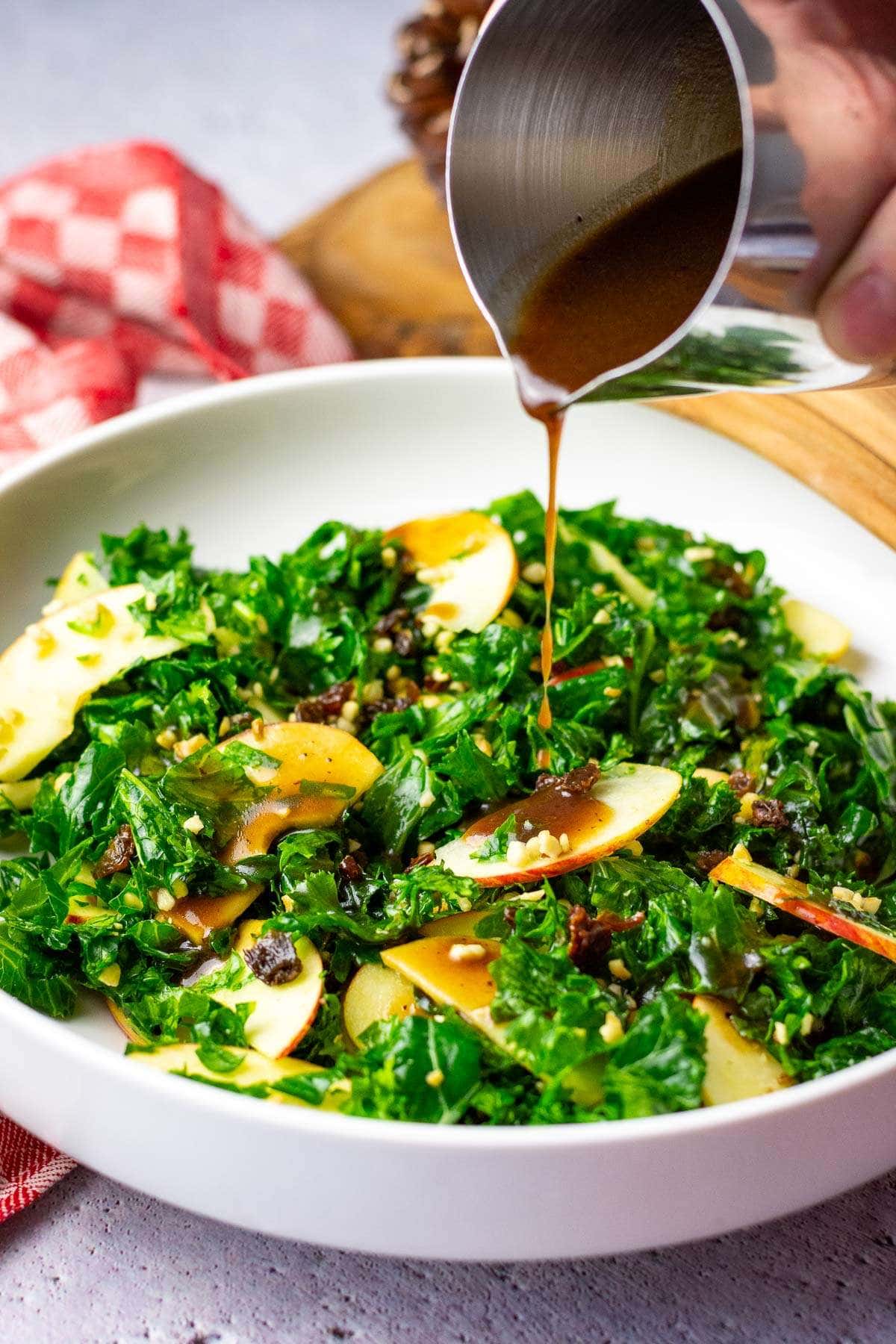 Pouring pomegranate molasses vinaigrette on kale, apple and walnut salad.