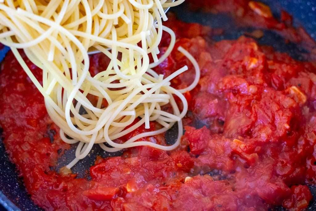 Adding cooked spaghetti to tomato sauce.