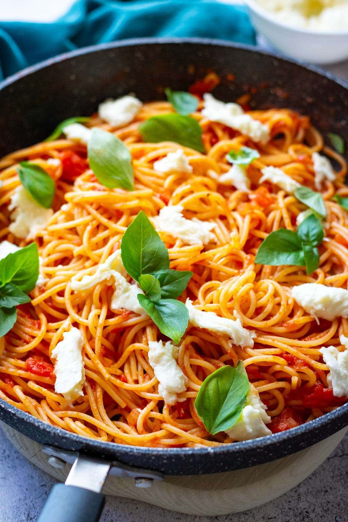 Tomato spaghetti with mozzarella garnished with basil in a large pan.