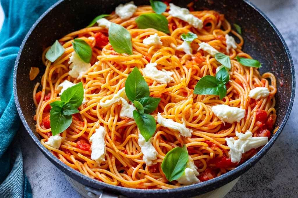 Tomato and mozzarella spaghetti topped with fresh basil leaves.