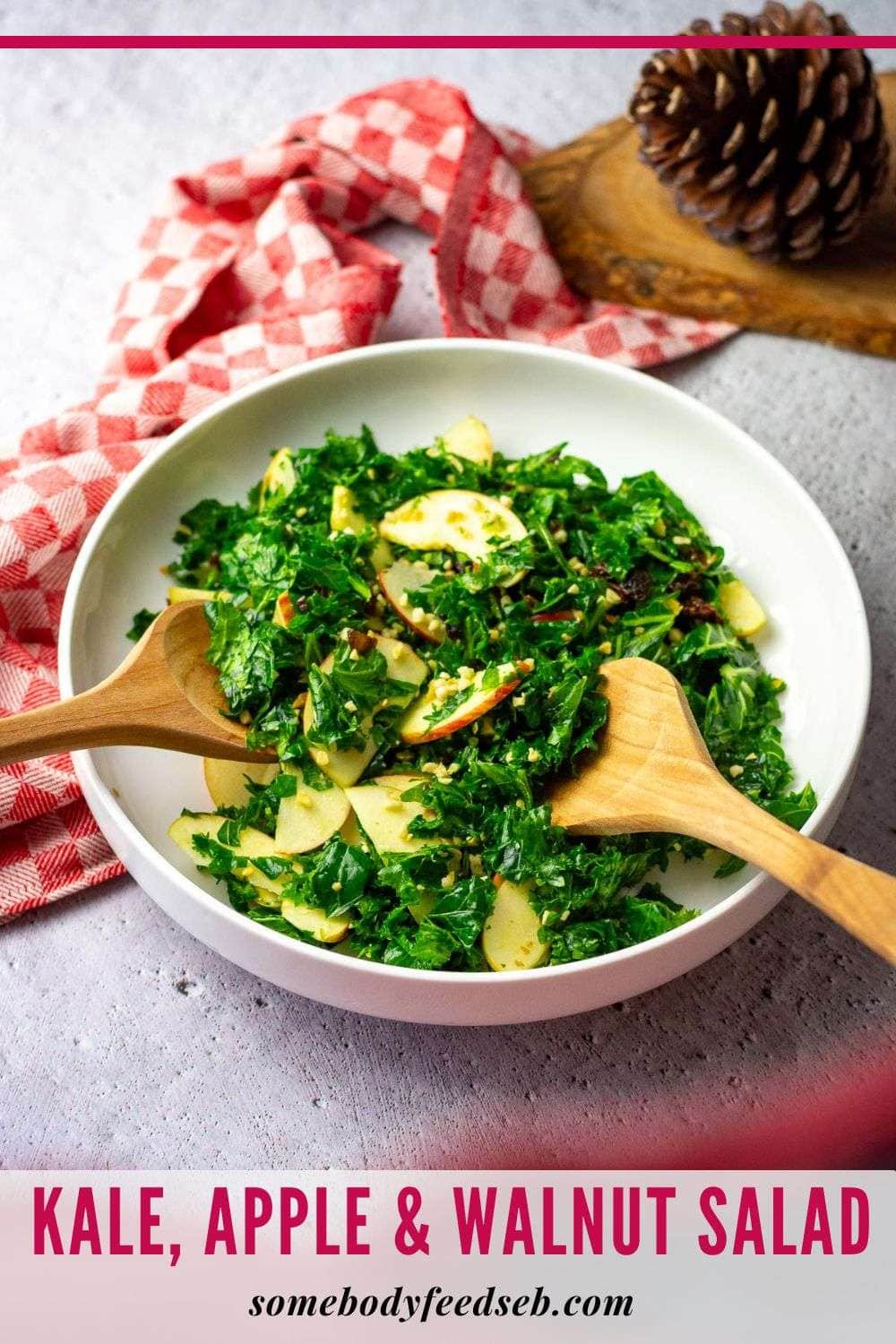 Kale, Apple and Walnut Salad being tossed in a white bowl with wooden serving spoons. - Pin for Pinterest.