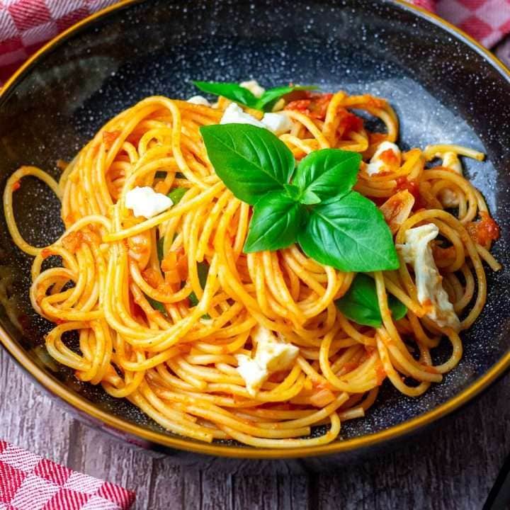 Tomato and Mozzarella pasta with basil in a black bowl.