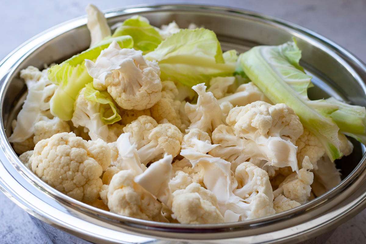 Cauliflower florets, chopped up stalk and leaves in a large metal bowl.