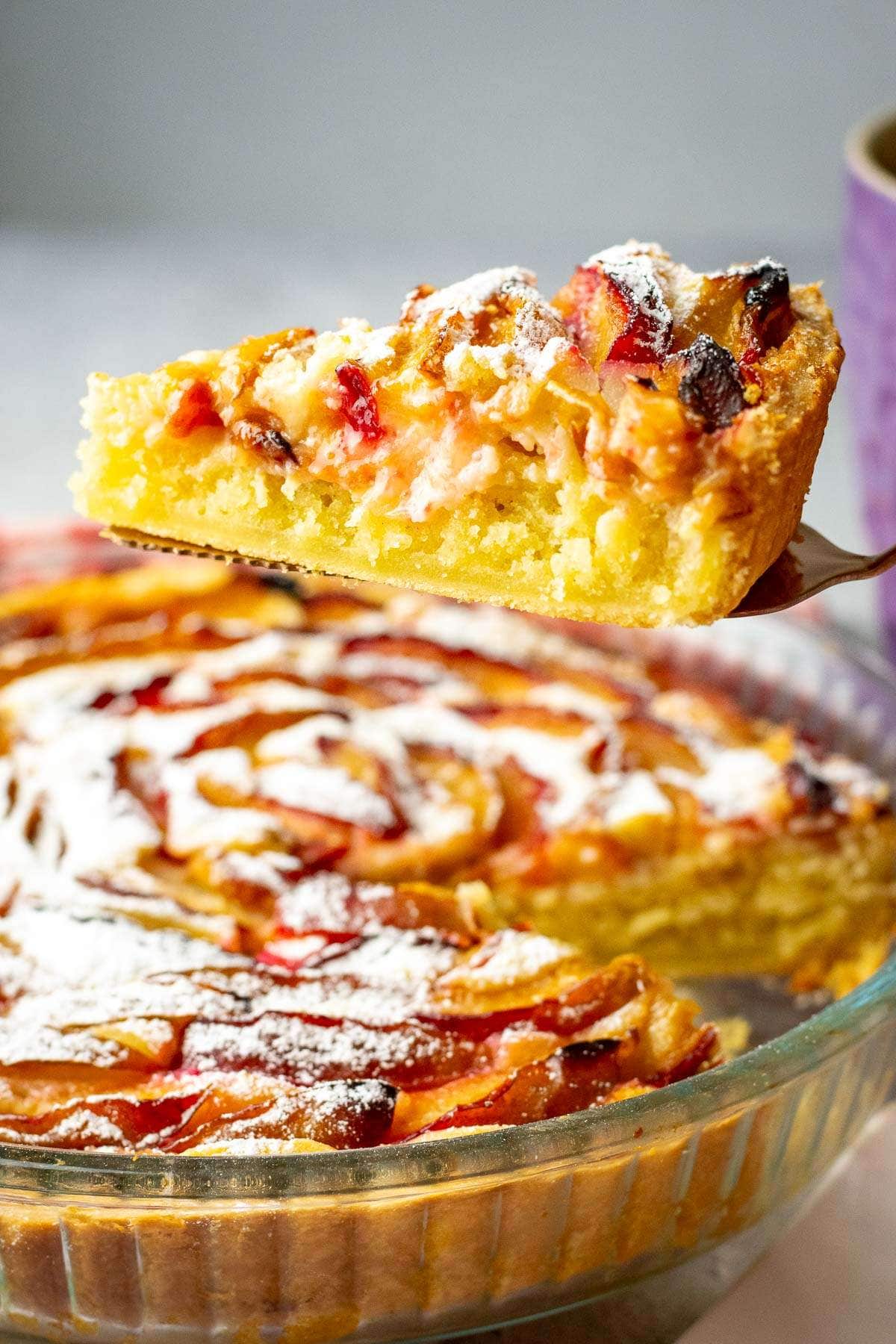 A slice of plum frangipane tart being lifted out of the tart tin.