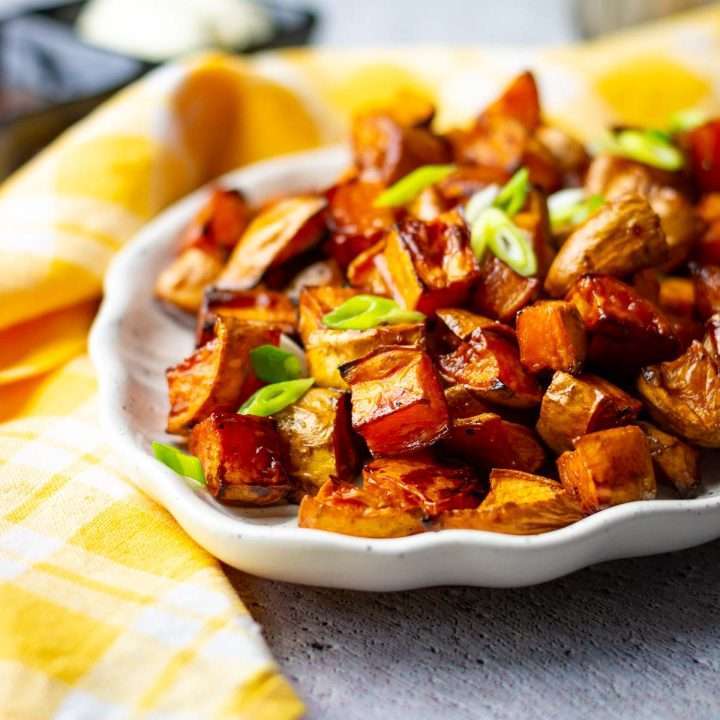 Balsamic Roasted Sweet Potatoes on a leaf-shaped white plate, garnihsed with spring onion.