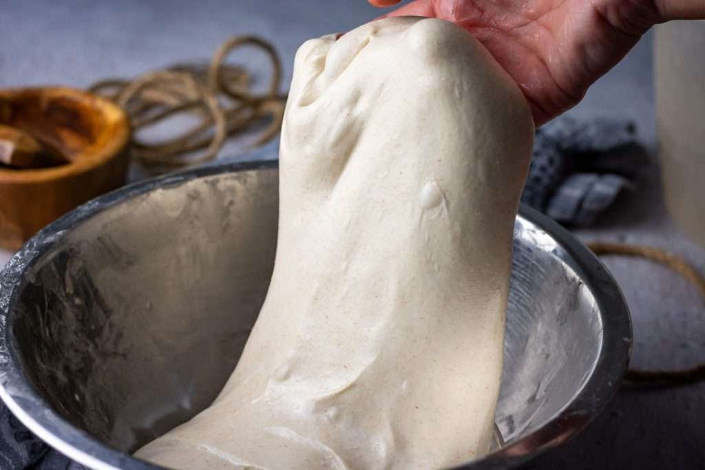 Sourdough in a metal bowl being pulled upwards without tearing.