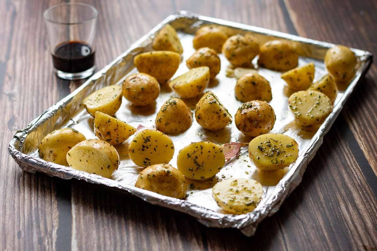 Halved babay potatoes covered in rosemary and oil on a baking tray,