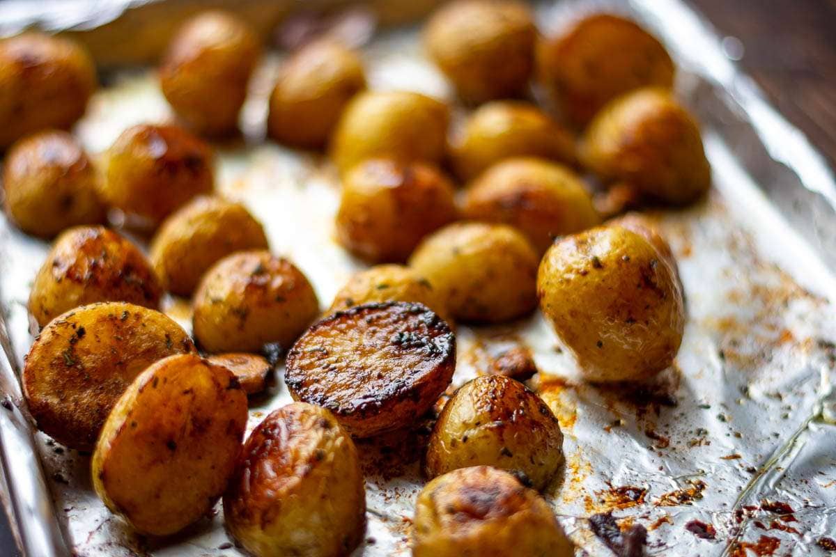 Roasted balsamic baby potatoes with caramelised edges on a baking tray lined with baking parchment.