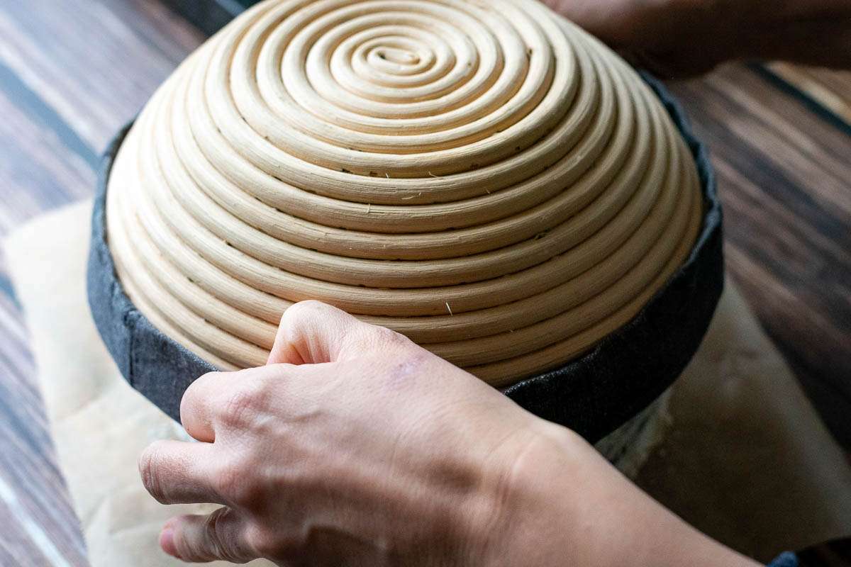 Inverting sourdough out of the banettone basket onto a piece of parchment paper.