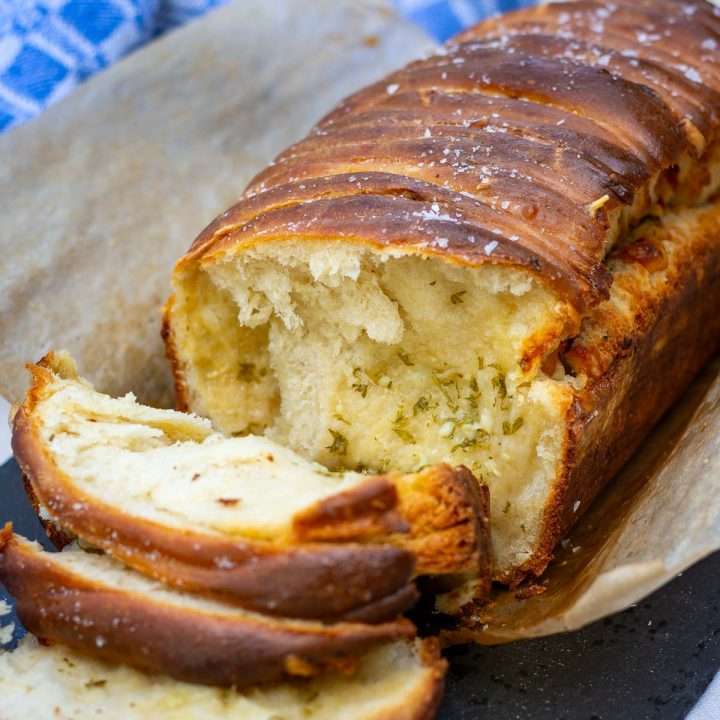 Sourdough pull-apart garlic bread with three slices already torn off exposing garlicy cheesy herby layer.