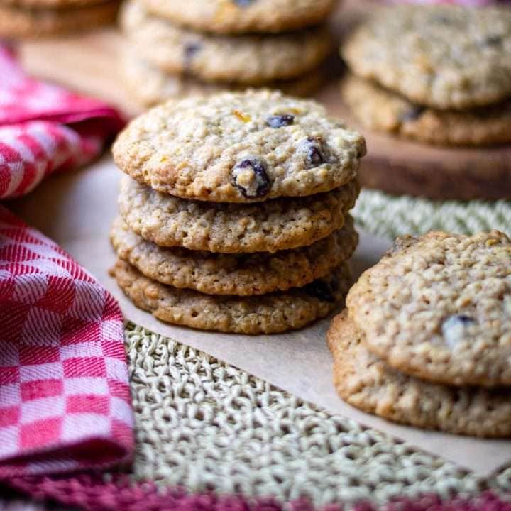 Stacked oatmeal raisin cookies on a piece of brown parchment paper.