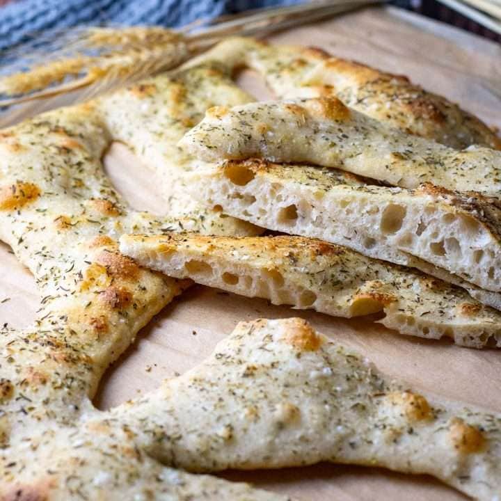 Sliced sourdough fougasse topped with herbs de provence on a sheet of parchment paper.