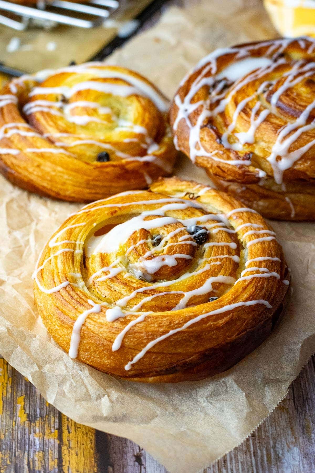 Glazed sourdough pains aux raisins on a sheet of parchment paper.