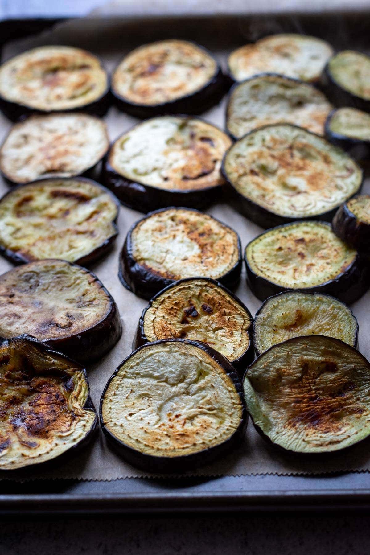 Browned aubergine slices on a large baking tray lined with parchment paper.