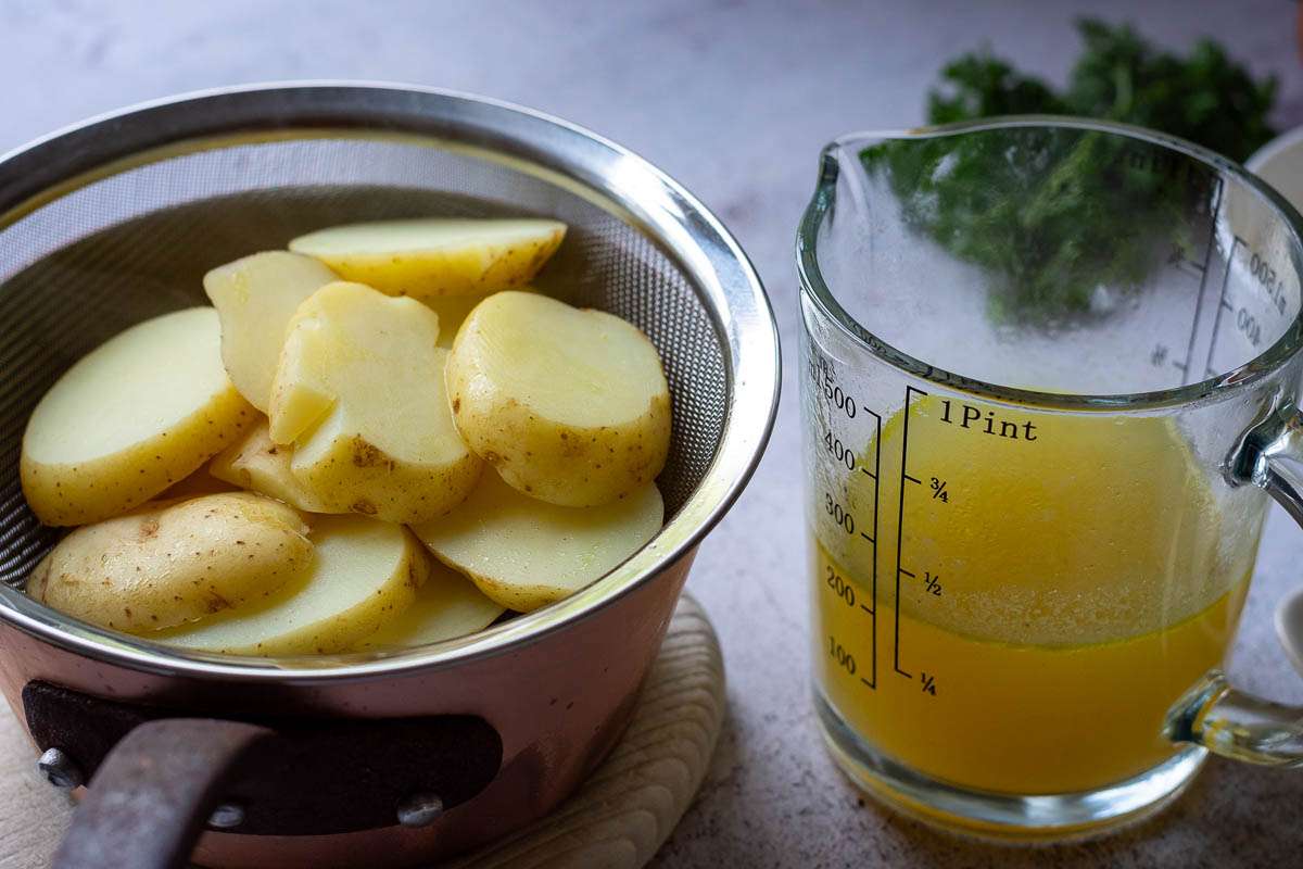 Boiled potato slices and stock in a jug next to each other.