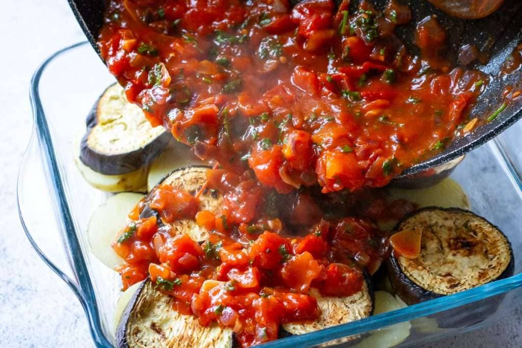 Tomato sauce is being poured over the aubergine and potatoes.